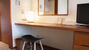 A hotel room with a wooden desk, a black chair, a mirror, a television, and a small trash bin. - Irou (Tonosho)