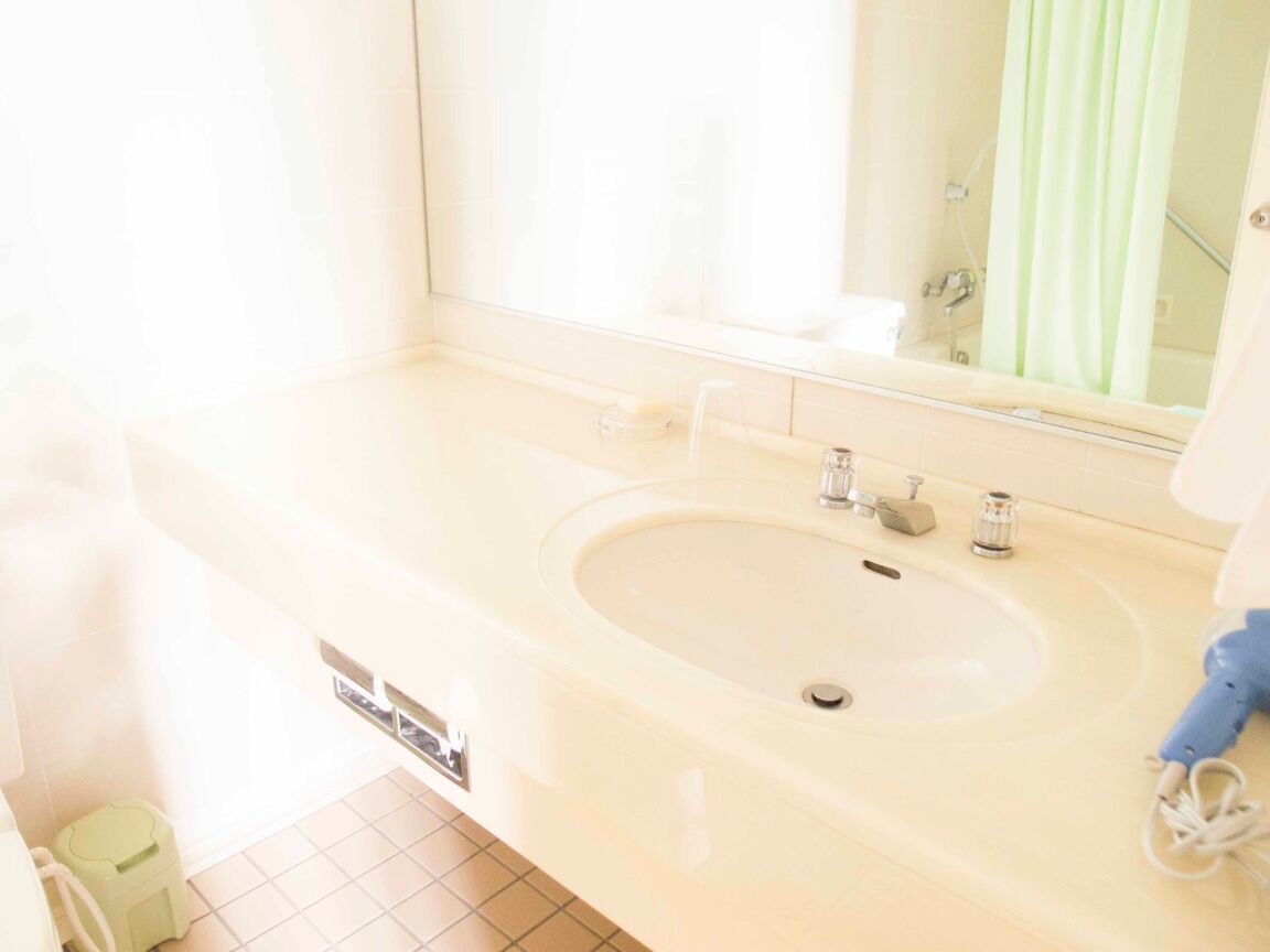 A bathroom with a large sink, mirror, and a green trash bin.
