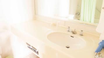 A bathroom with a large sink, mirror, and a green trash bin.