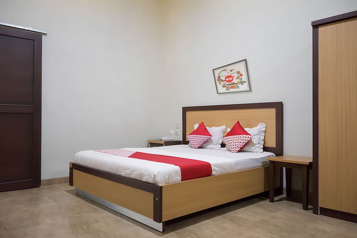 Una cama bien hecha con estructura de madera y ropa de cama blanca, dos mesitas de noche, un armario de madera y un cuadro enmarcado en la pared.