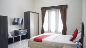 Een hotelkamer met een bed, een televisie, een kledingkast en een raam met gordijnen.