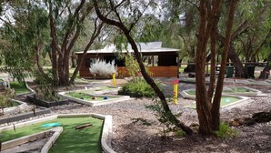 Un campo de mini golf con un club house de madera, rodeado de árboles y zonas ajardinadas.