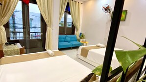 Habitación de hotel con dos camas, un sofá azul, una mesita con un cuenco y un ventilador en la pared.