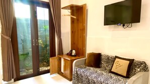 Una habitación moderna con puerta de vidrio que da a un jardín interior, un armario de madera, un sofá estampado de leopardo y un televisor de pantalla plana montado en la pared.