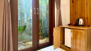 Habitación con puerta corrediza de vidrio que da a un jardín, muebles de madera y una tetera sobre la encimera.