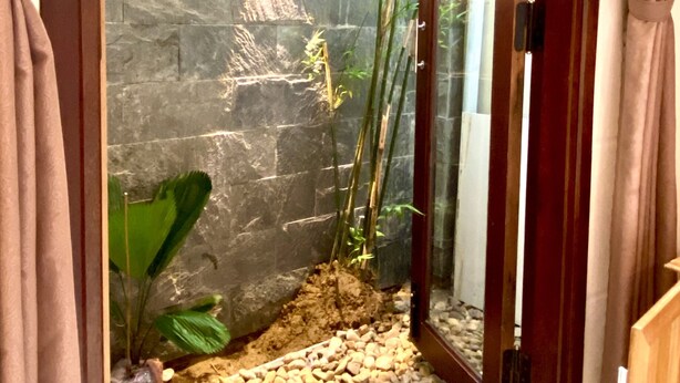 Una habitación con pared de piedra, planta de bambú y una pequeña zona de guijarros.