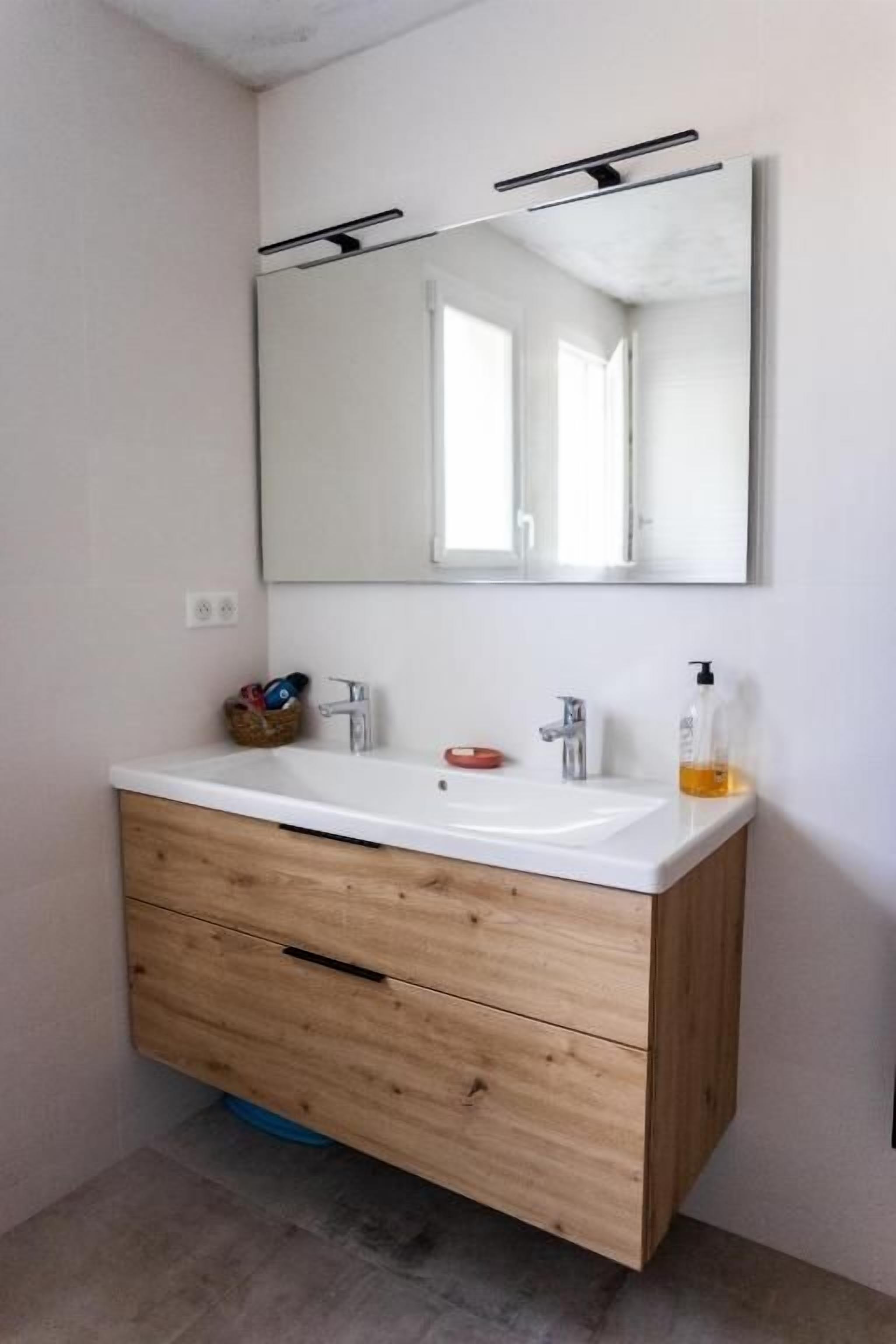 A bathroom with a white vanity, wooden cabinet, and a large mirror.