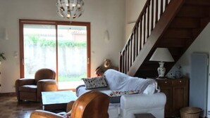 Een ruime woonkamer met houten vloeren, een bank, een fauteuil en een trap.