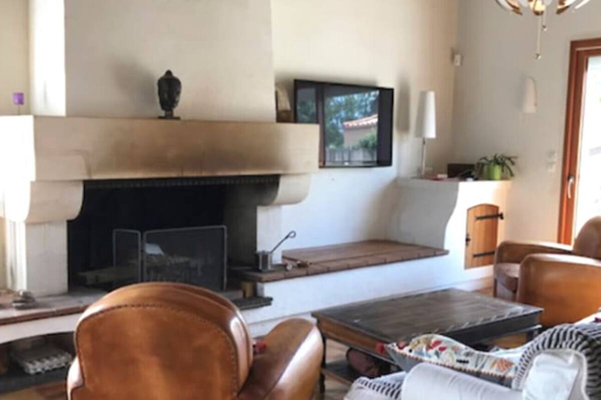 Een woonkamer met een open haard, een leren fauteuil, een witte bank en een houten salontafel.