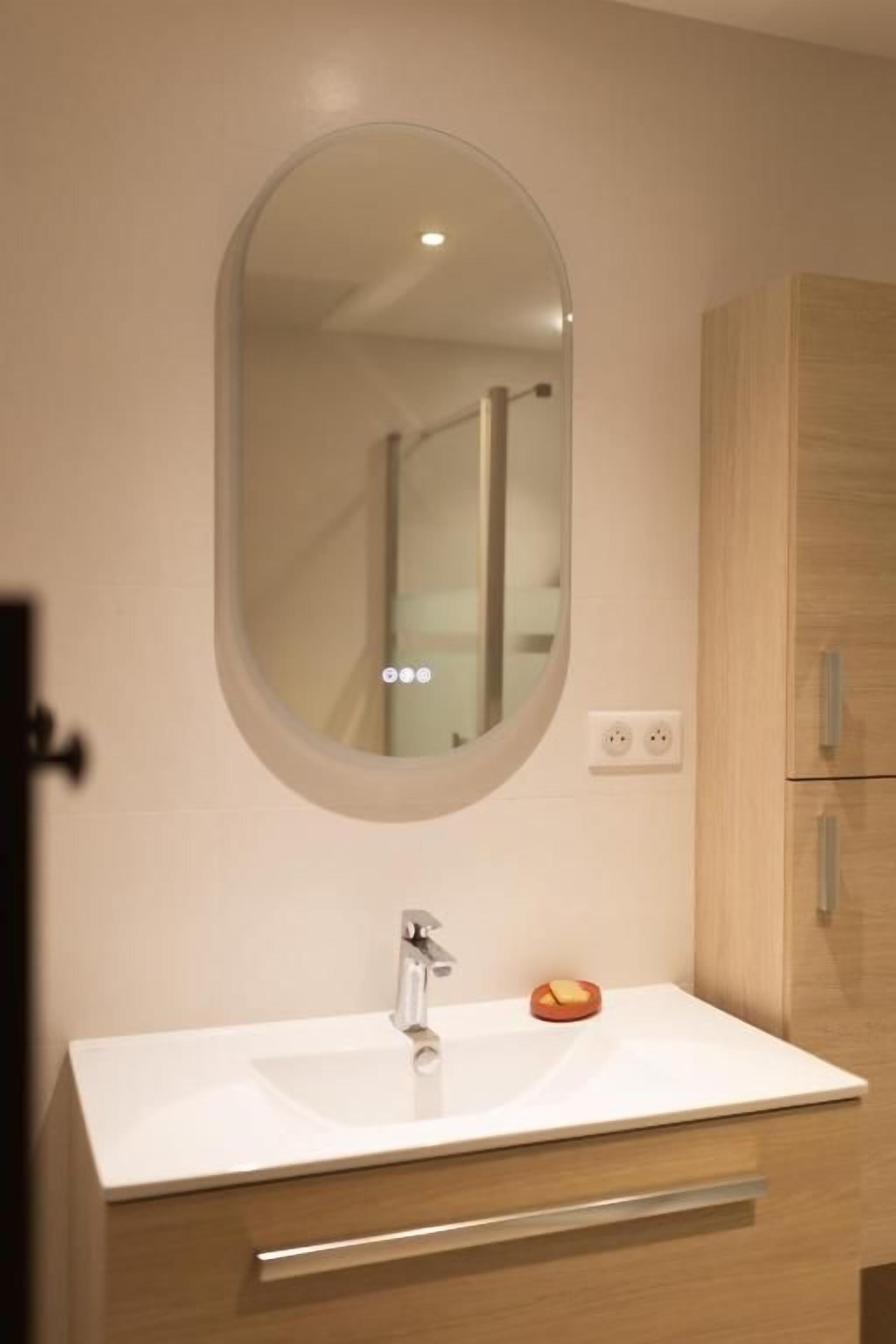 Un baño con un lavamanos blanco, un espejo redondo y un mueble de madera.