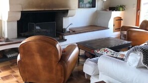 Een gezellige woonkamer met een open haard, een leren fauteuil, een witte bank en een houten salontafel.