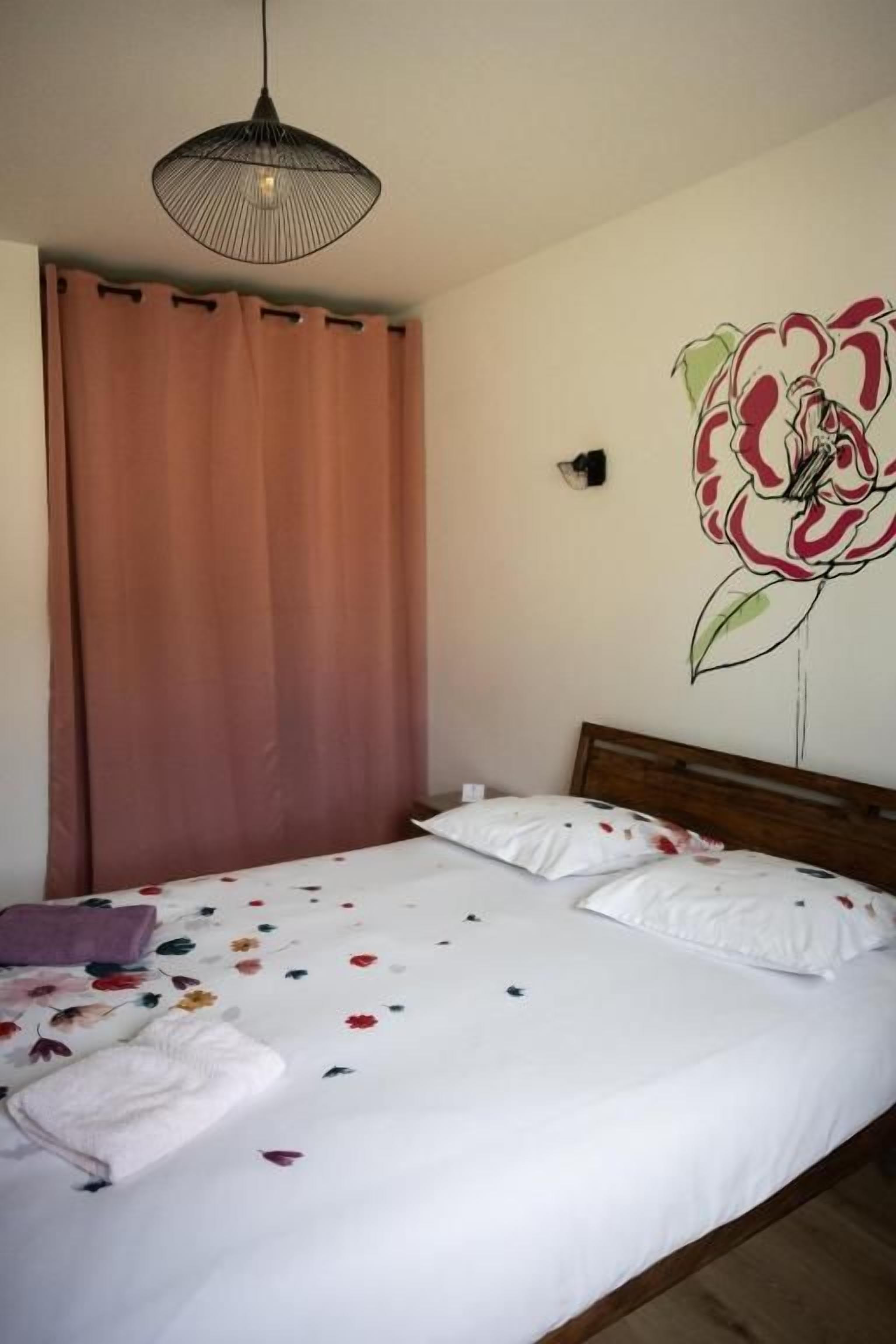 A bedroom with a bed, a hanging light fixture, a wall-mounted artwork, and a window with curtains.