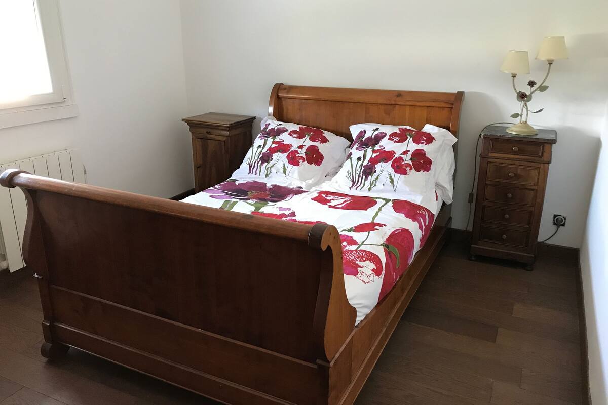 Een houten bed met een bloemenprint sprei, een nachtkastje en een bijzettafeltje met lampen.