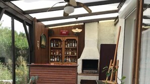 Een overdekt terras met een bar, zitplaatsen en een open haard.