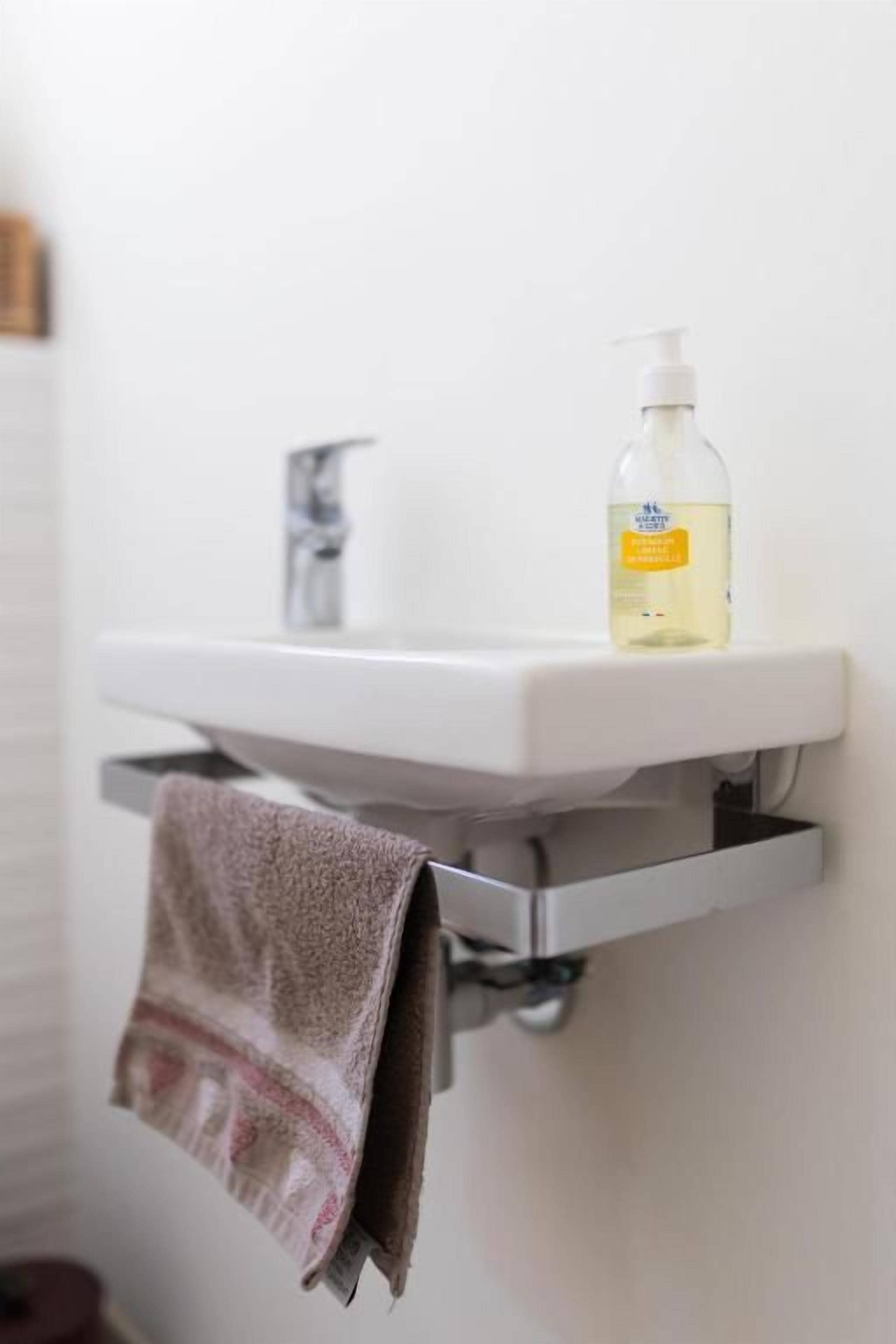 Un lavamanos de baño con una botella de jabón líquido y una toalla colgada en un perchero.