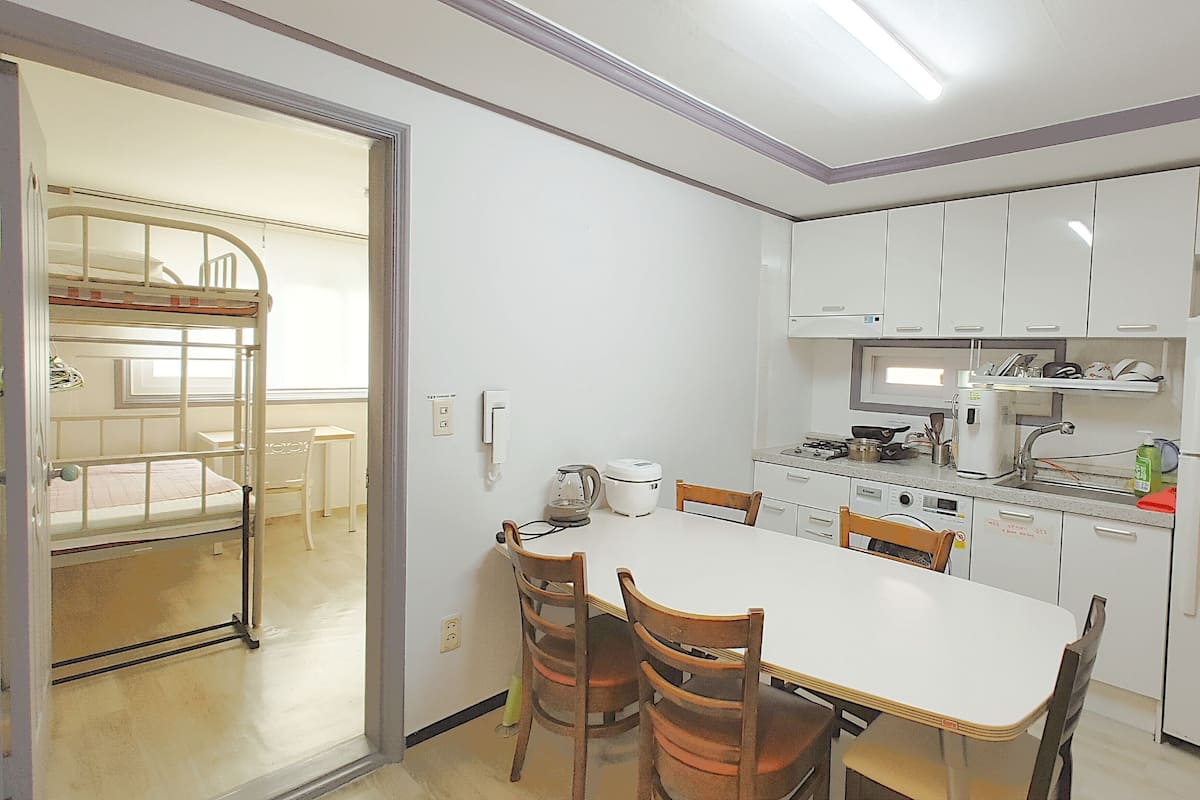 Una cocina compacta con armarios blancos, una mesa de comedor con sillas, una estufa integrada y un refrigerador.