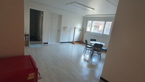 Una habitación amplia con suelo de madera, una mesa de comedor con sillas, un refrigerador rojo y una puerta que da a otra habitación.