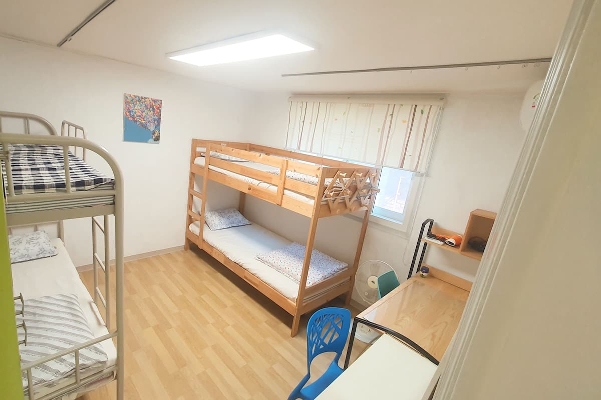 Un dormitorio con literas, dos camas dobles, un escritorio, una silla, un ventilador y una ventana con cortinas.