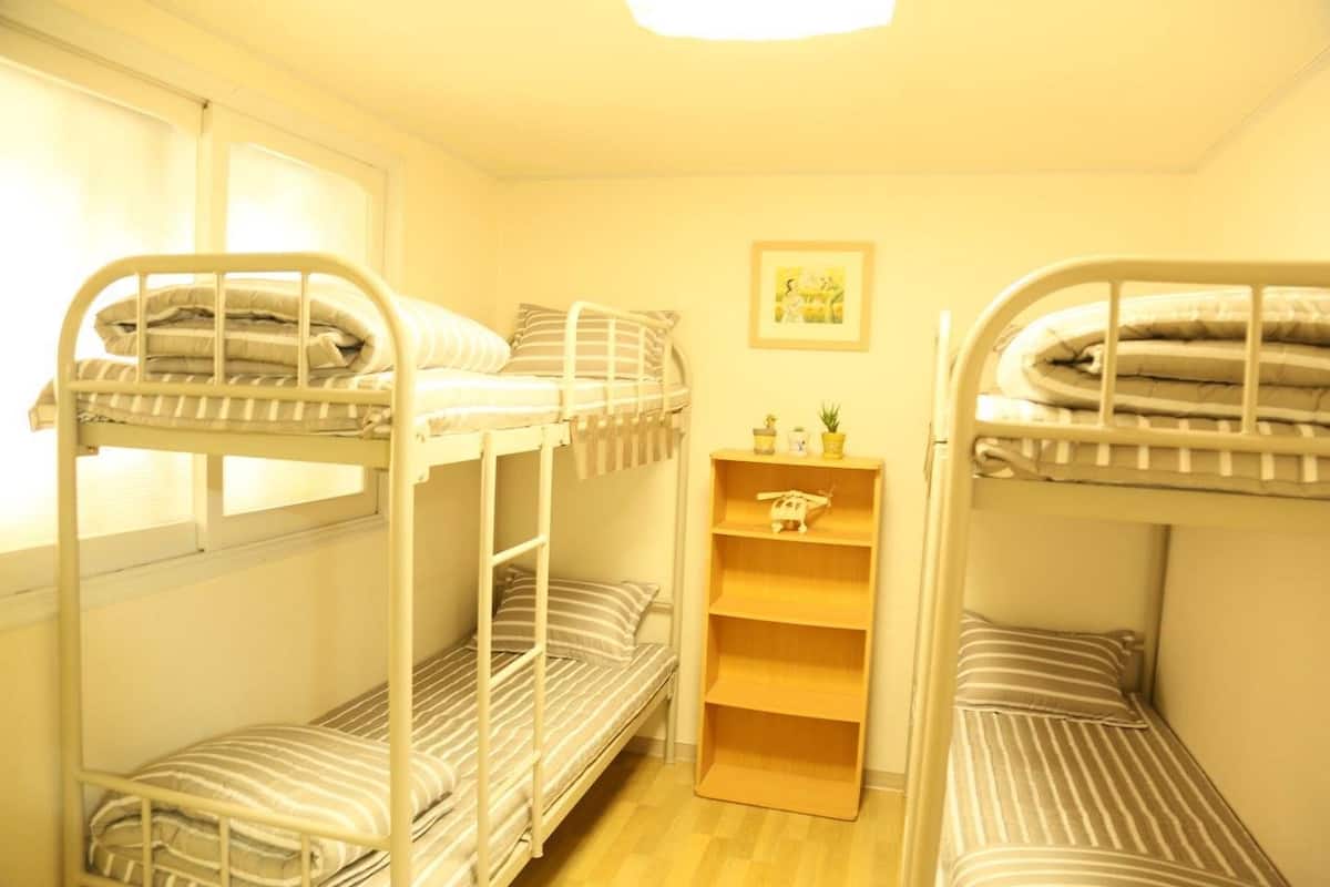 Un dormitorio con literas, un estante pequeño con objetos decorativos y una ventana.