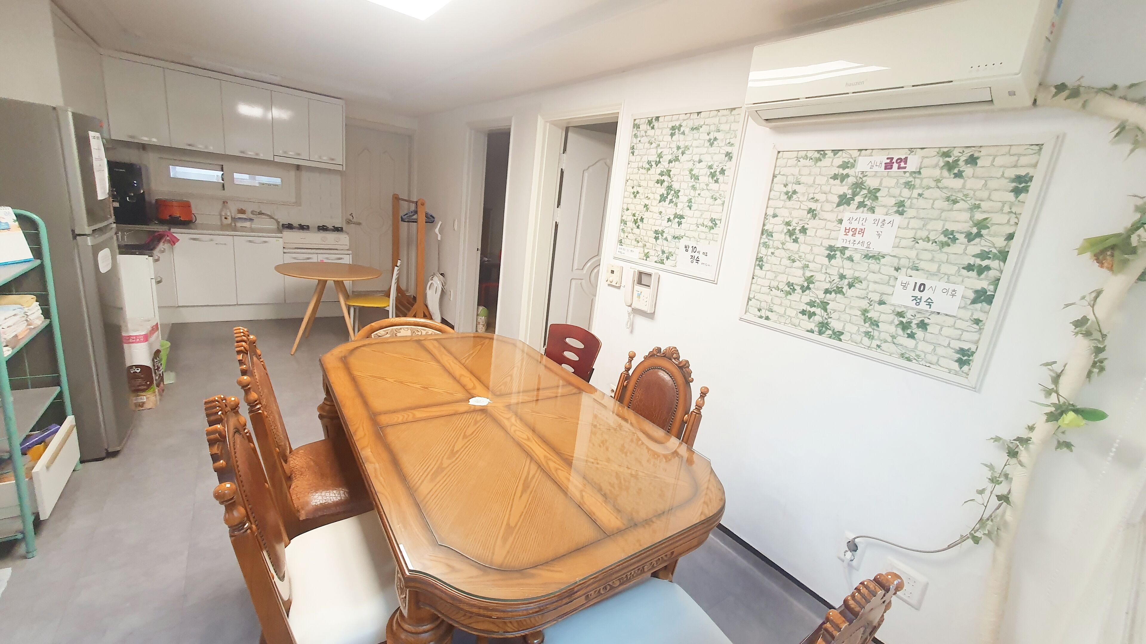 A dining area with a wooden table and chairs, a kitchen in the background, and a wall with a decorative pattern.