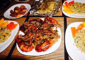 A table with various dishes including grilled seafood, fried plantains, and rice. - Sunset view beach hotel (Arugam Bay)
