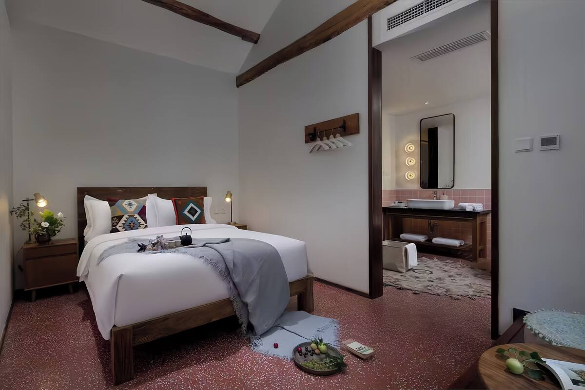 Een moderne slaapkamer met een houten bed, nachtkastjes met lampen, een kleine plant en een fruitschaal.