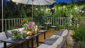 Une terrasse extérieure avec une table à manger placée sous un grand parasol, entourée de chaises et de plantes en pot.