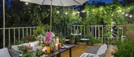An outdoor patio with a dining table set under a large umbrella, surrounded by chairs and potted plants.