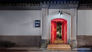 Une entrée d’immeuble de style traditionnel, avec une arche rouge, une enseigne indiquant « PEKING YARD » et un toit recouvert de tuiles.