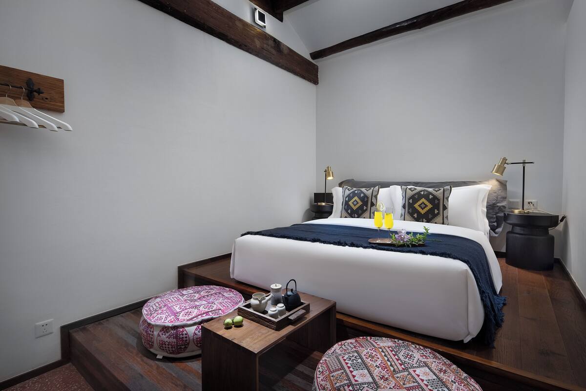 Een moderne slaapkamer met een groot bed, nachtkastjes, een lamp en een klein bijzettafeltje met decoratieve objecten.
