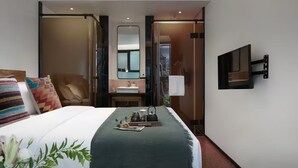 Une chambre d’hôtel équipée d’un lit, d’une table de chevet, d’un miroir, d’une télévision et offrant une vue sur l’extérieur.