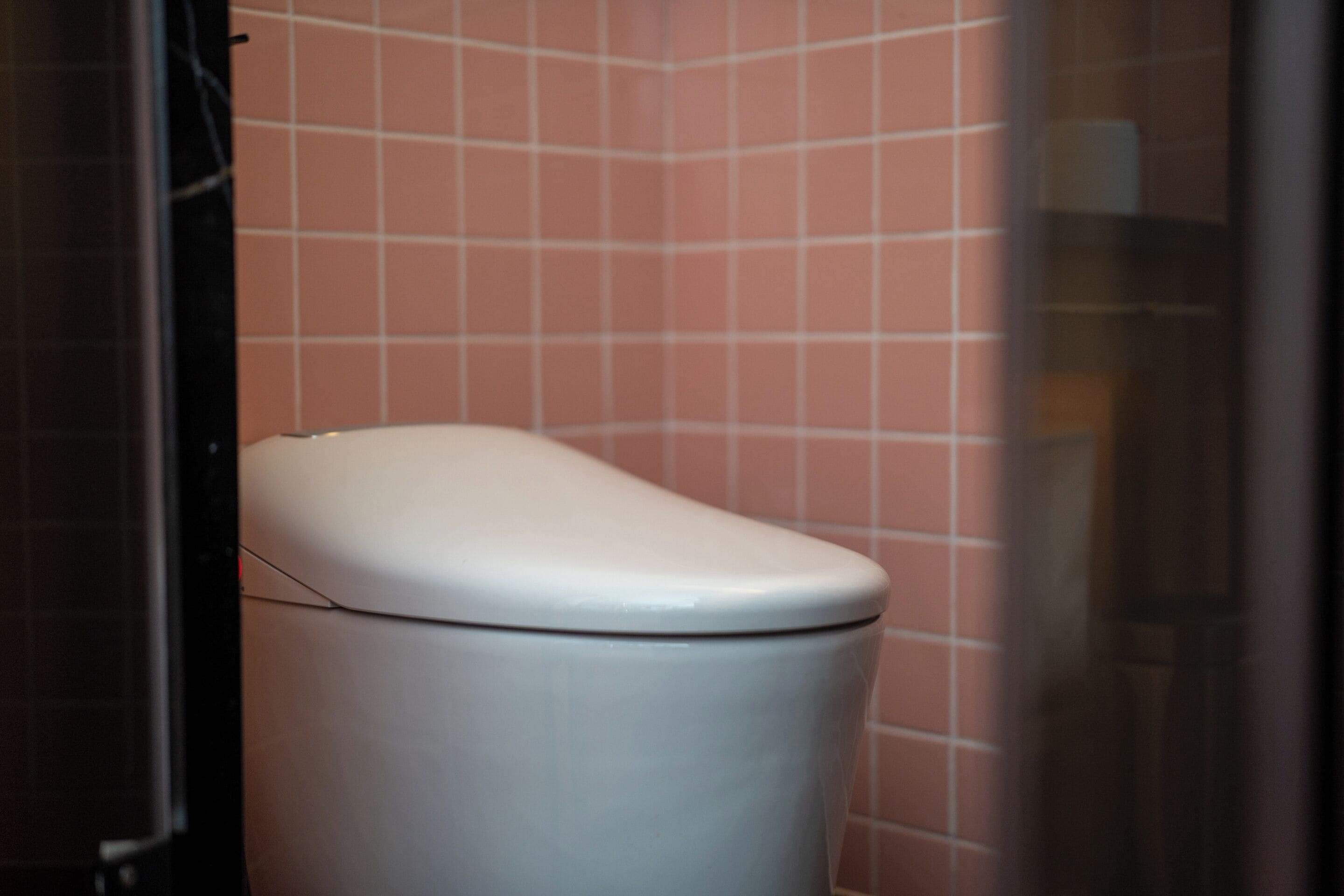 Eine weiße Toilette in einem Badezimmer mit rosa gefliesten Wänden.