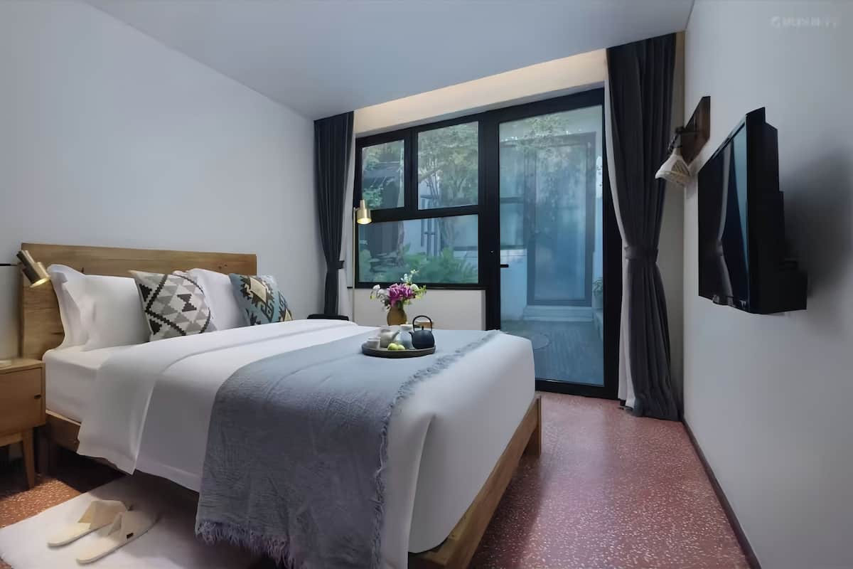 Een hotelkamer met een groot bed, een nachtkastje, een raam met gordijnen en een aan de muur bevestigde televisie.