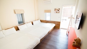 Quarto de hotel com uma cama grande, piso de madeira, uma janela pequena, televisão presa à parede e um urso de pelúcia em cima de uma mesa.