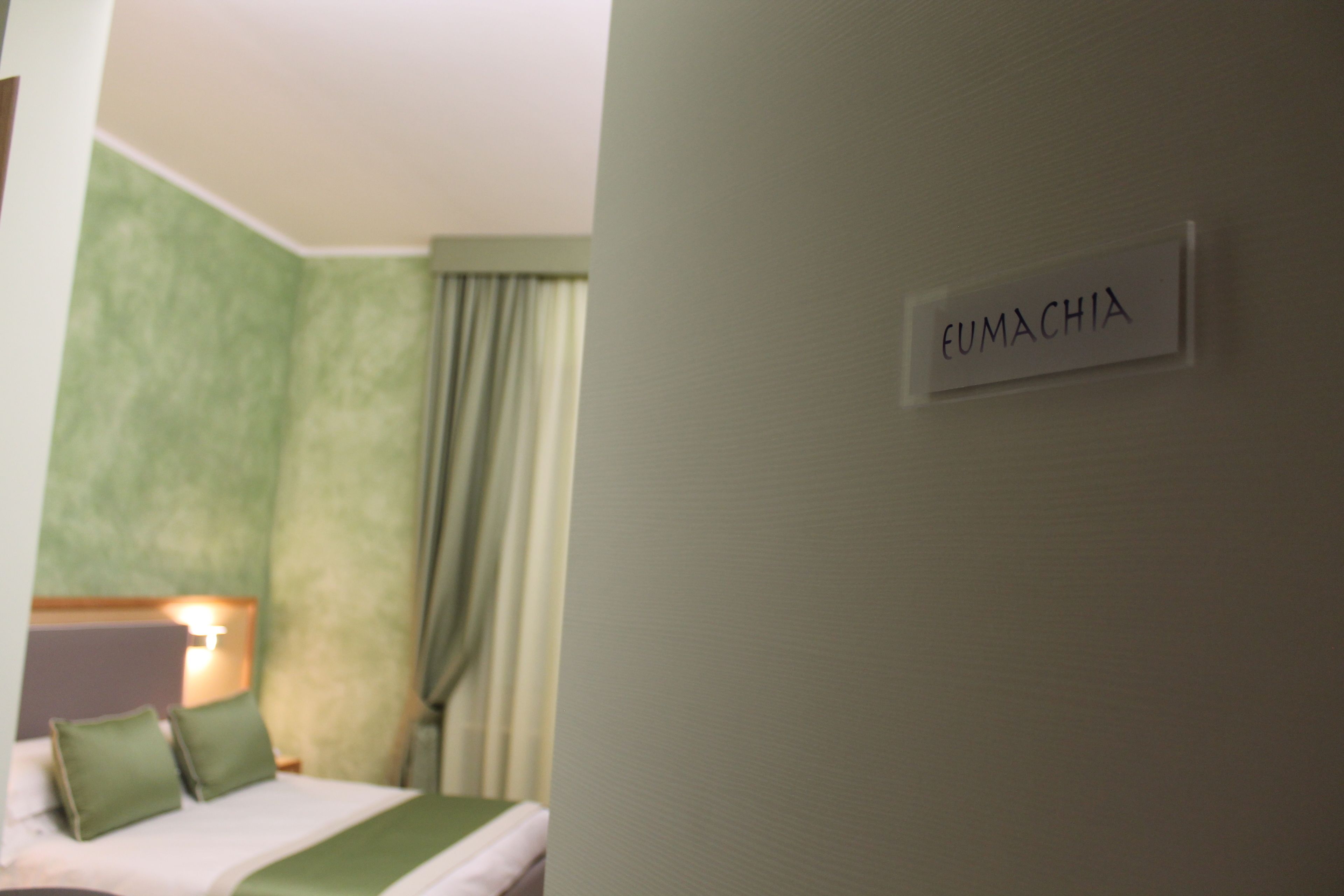 Habitación de hotel con una cama, una mesita de noche y un cartel en la pared que dice 'FUMACHIA'.