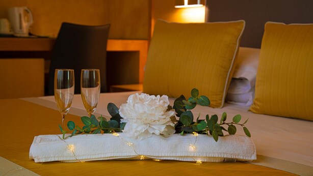 A neatly made bed with two pillows, a bedside table with a lamp, and two glasses of champagne on a table. - B&B Lapillus (Pompei)