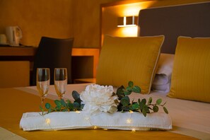A neatly made bed with two pillows, a bedside table with a lamp, and two glasses of champagne on a table. - B&B Lapillus (Pompei)