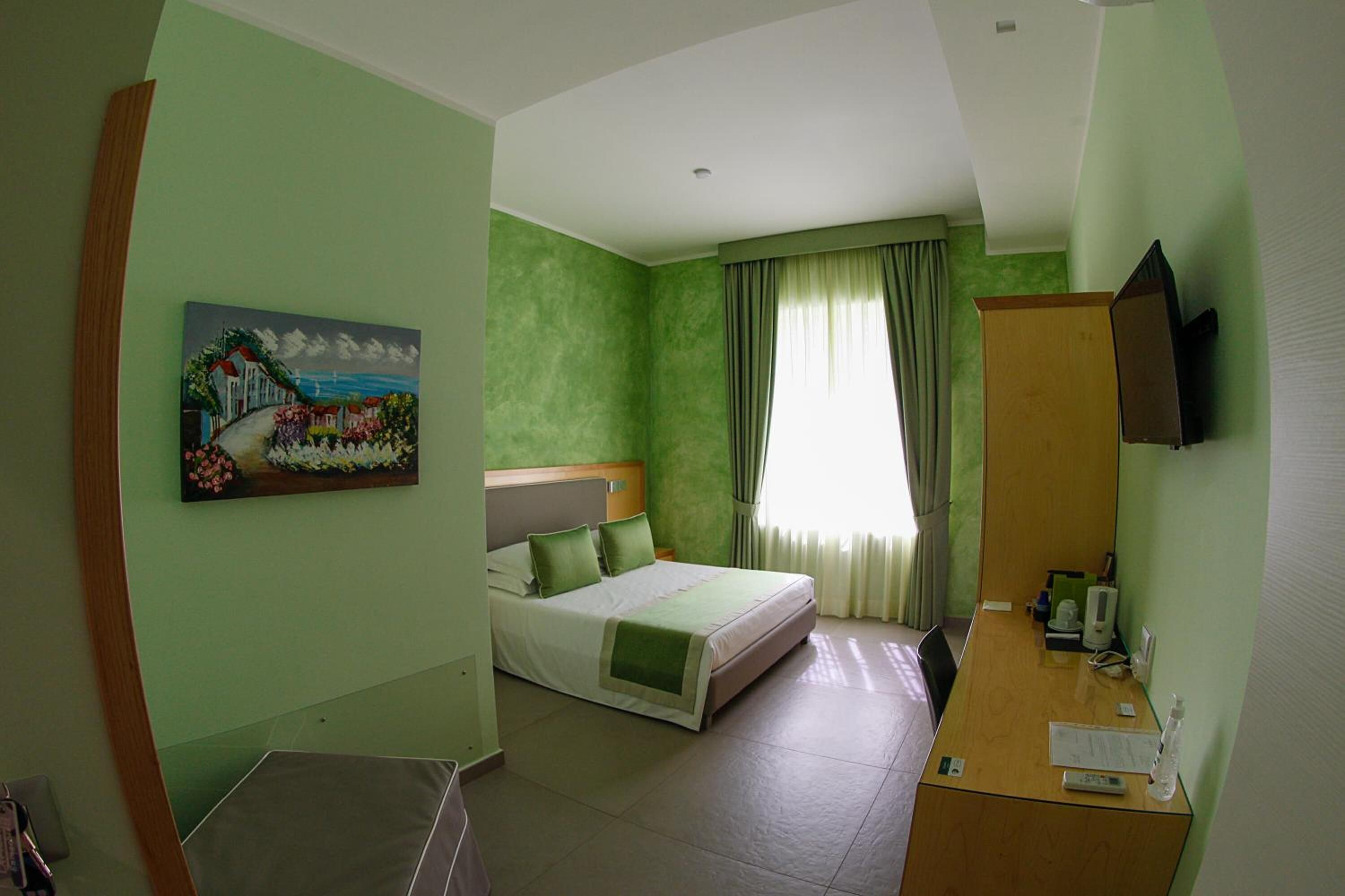 Una habitación de hotel con una cama, un escritorio, un televisor y un cuadro en la pared.