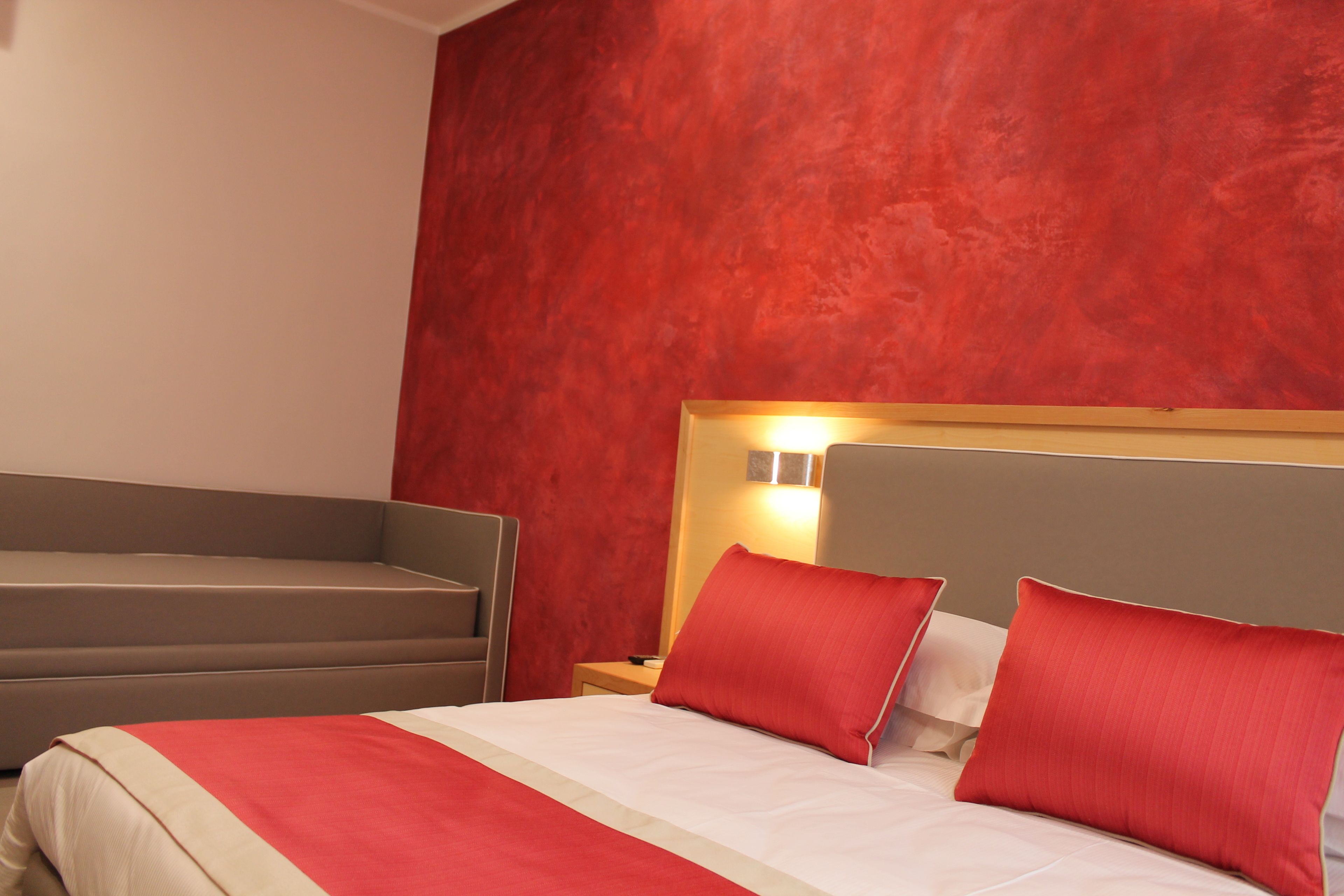 Habitación de hotel con una cama, una mesita de noche y una pared de acento roja.