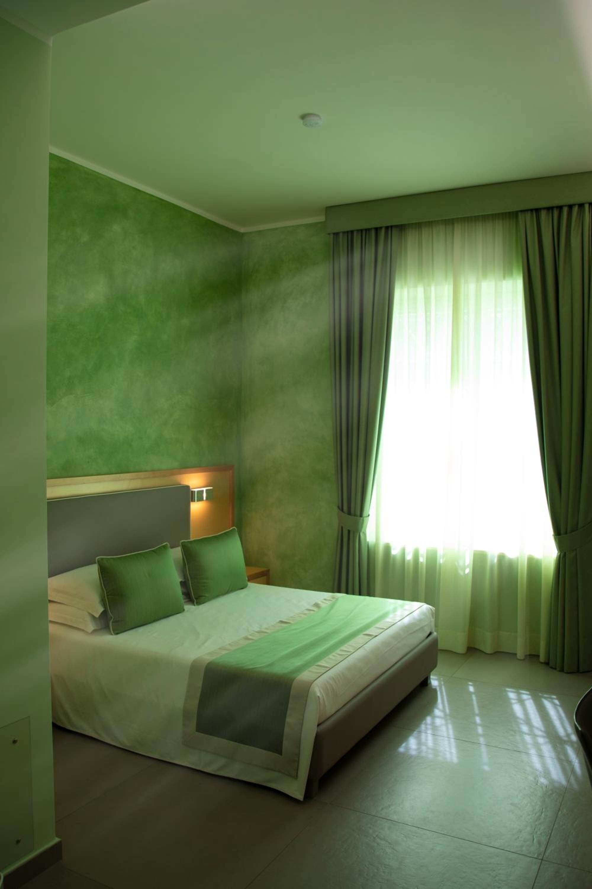 A hotel room with a large bed, green walls, and a window with curtains.