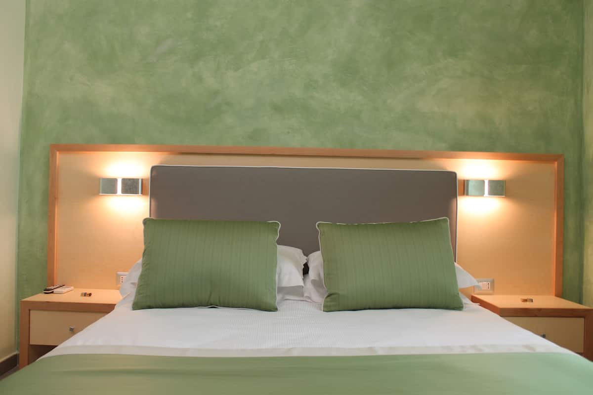 A neatly made bed with green pillows and a wooden headboard, flanked by nightstands with lamps.