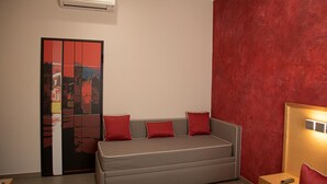 A modern bedroom with a grey sofa, red cushions, a wooden bedside table, and a red textured wall. - B&B Lapillus (Pompei)