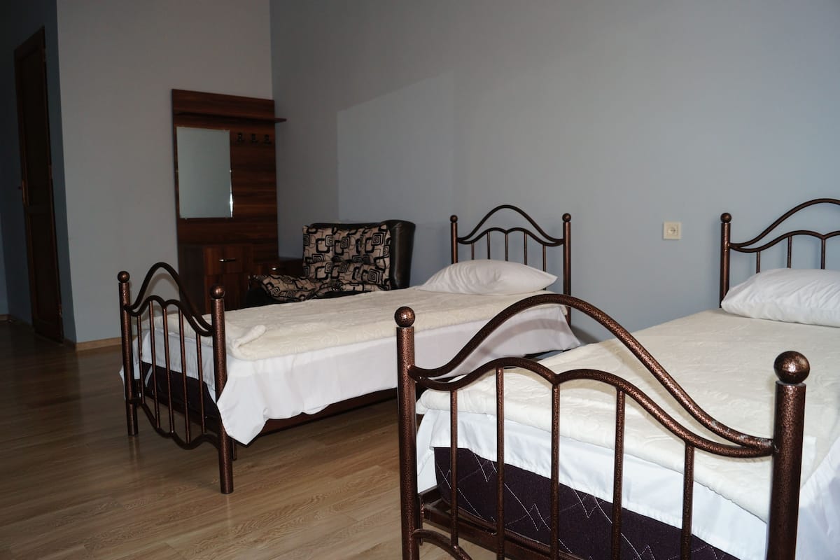 A room with two wooden beds, a wooden chair, a mirror, and a wooden floor.