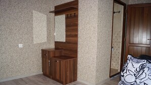 Ein Zimmer mit einem Holzschrank, einem Spiegel, einem gemusterten Sofa und einer Tür mit geometrischem Muster.