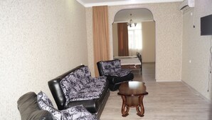 Ein Wohnzimmer mit Sofa, Sessel und Couchtisch, ein Essbereich mit Tisch und Stühlen sowie ein Flur, der zum Schlafzimmer führt.