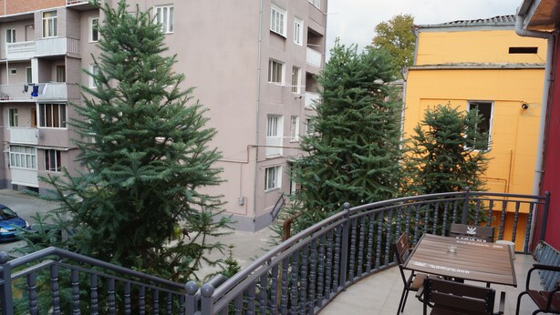 Ein Balkon mit Tisch und Stühlen, umgeben von einem Geländer, mit Blick auf eine Wohngegend mit Bäumen und Gebäuden.
