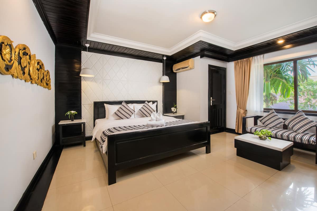 Quarto moderno com cama preta, sofá branco e uma grande janela com cortinas.