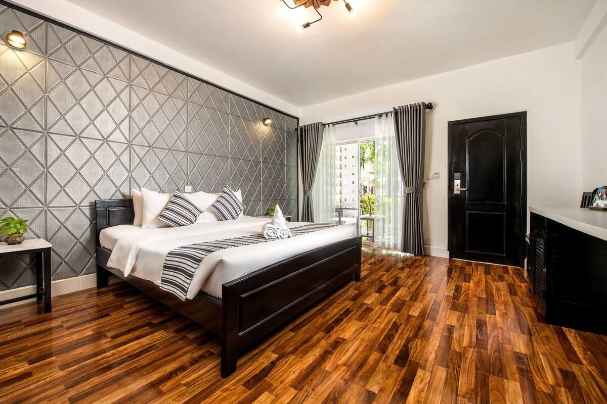Quarto moderno com uma cama grande, cabeceira com padrão geométrico e piso de madeira.
