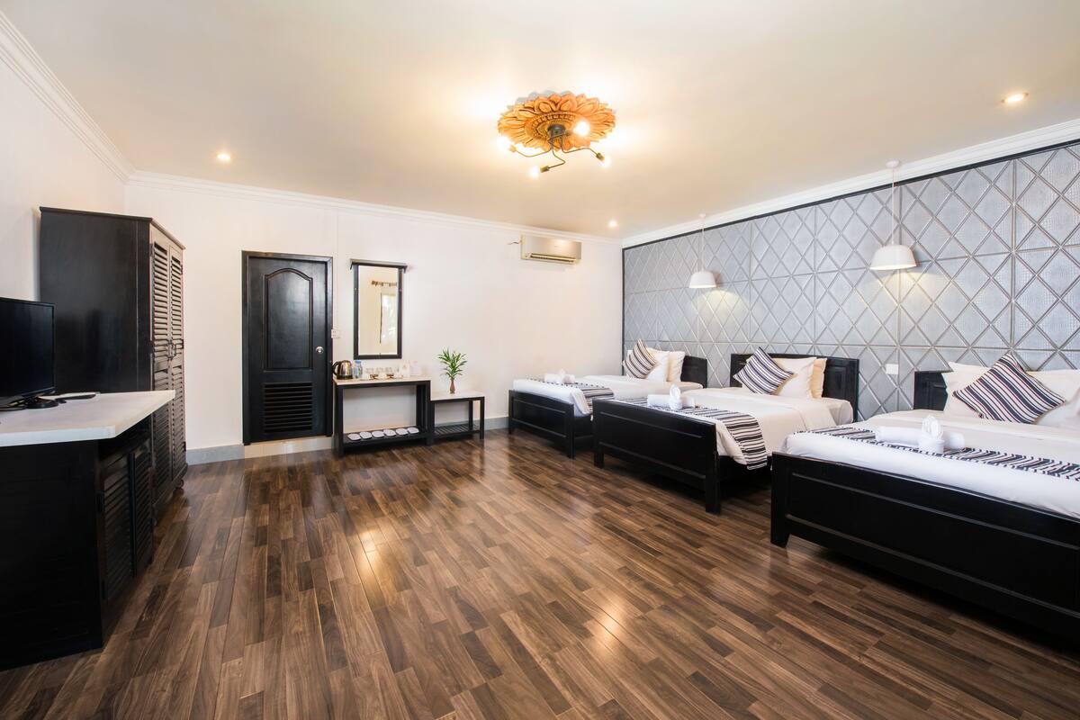 Quarto de hotel moderno com piso de madeira, uma cama grande, uma cama menor, uma escrivaninha e uma televisão.