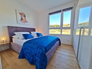 A bedroom with a bed, a nightstand, a window, and a painting on the wall. - StellaMare Apartments (Split)